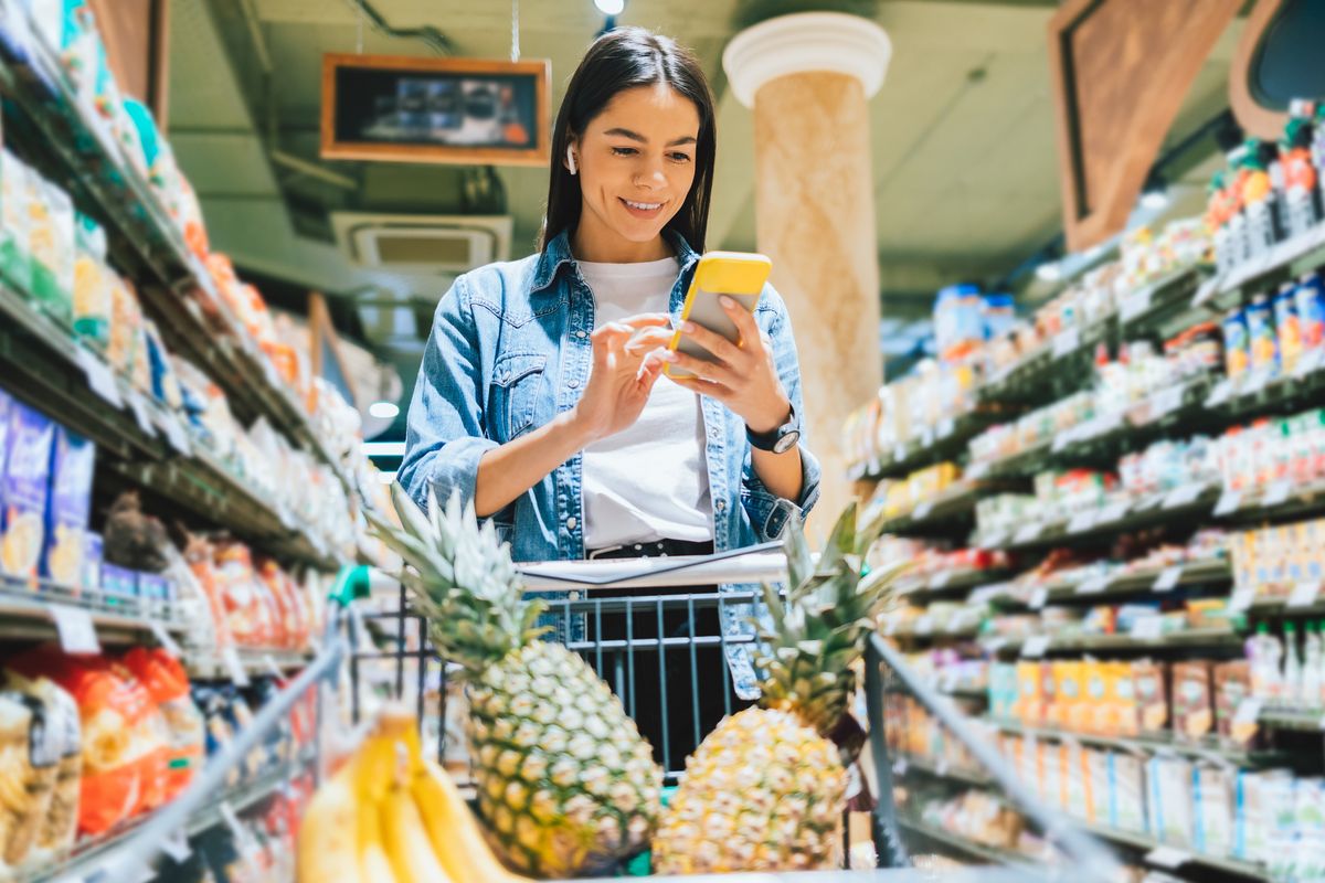 ragazza che fa la spesa con lo smartphone in mano e l'ananas nel carrello