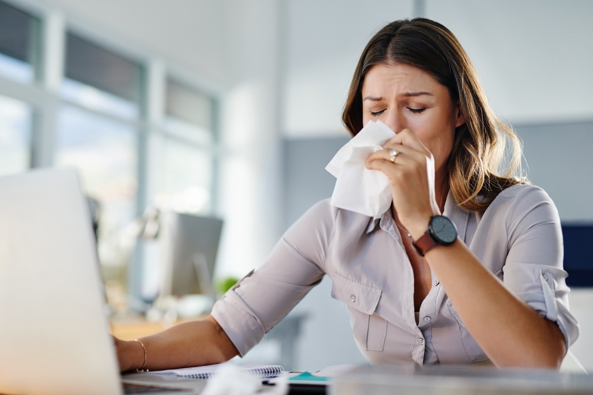 Una donna seduta al computer si soffia il naso per colpa dell'allergia