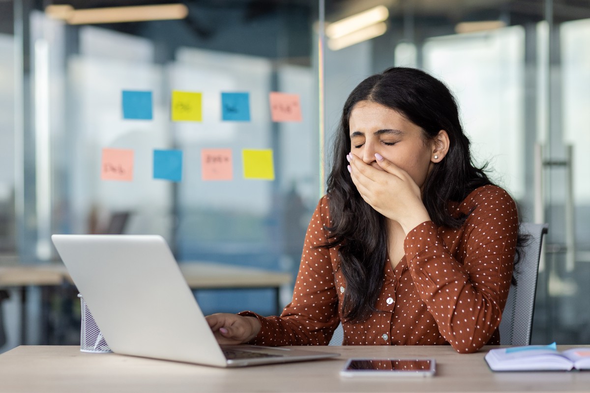 Una donna in ufficio che si stira e sbadiglia mentre lavora