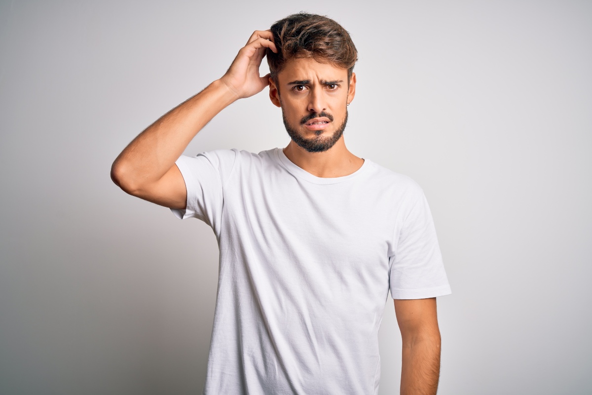 Giovane uomo in atteggiamento pensieroso si tocca la testa